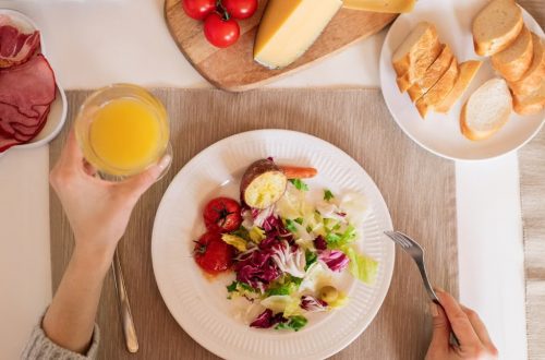 A top-view of a delicious breakfast setting featuring a salad, bread, cheese, tomatoes, and orange juice.